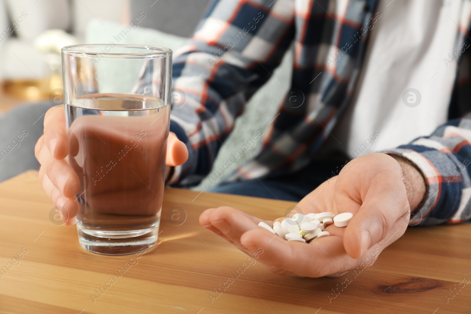 Photo of Man holding pills and glass of water at table, closeup