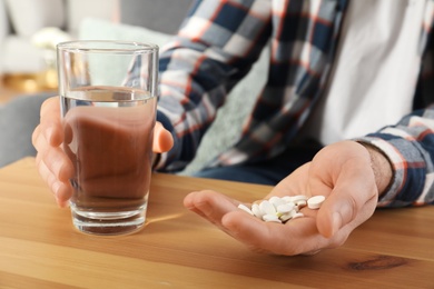 Man holding pills and glass of water at table, closeup