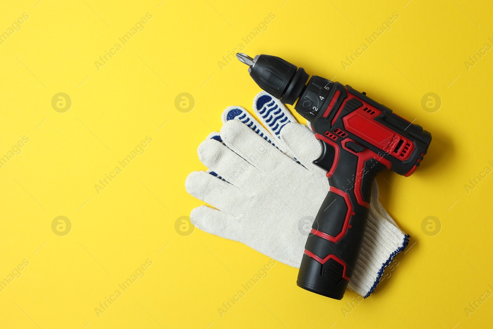 Photo of Electric screwdriver, bit set and gloves on yellow background, flat lay