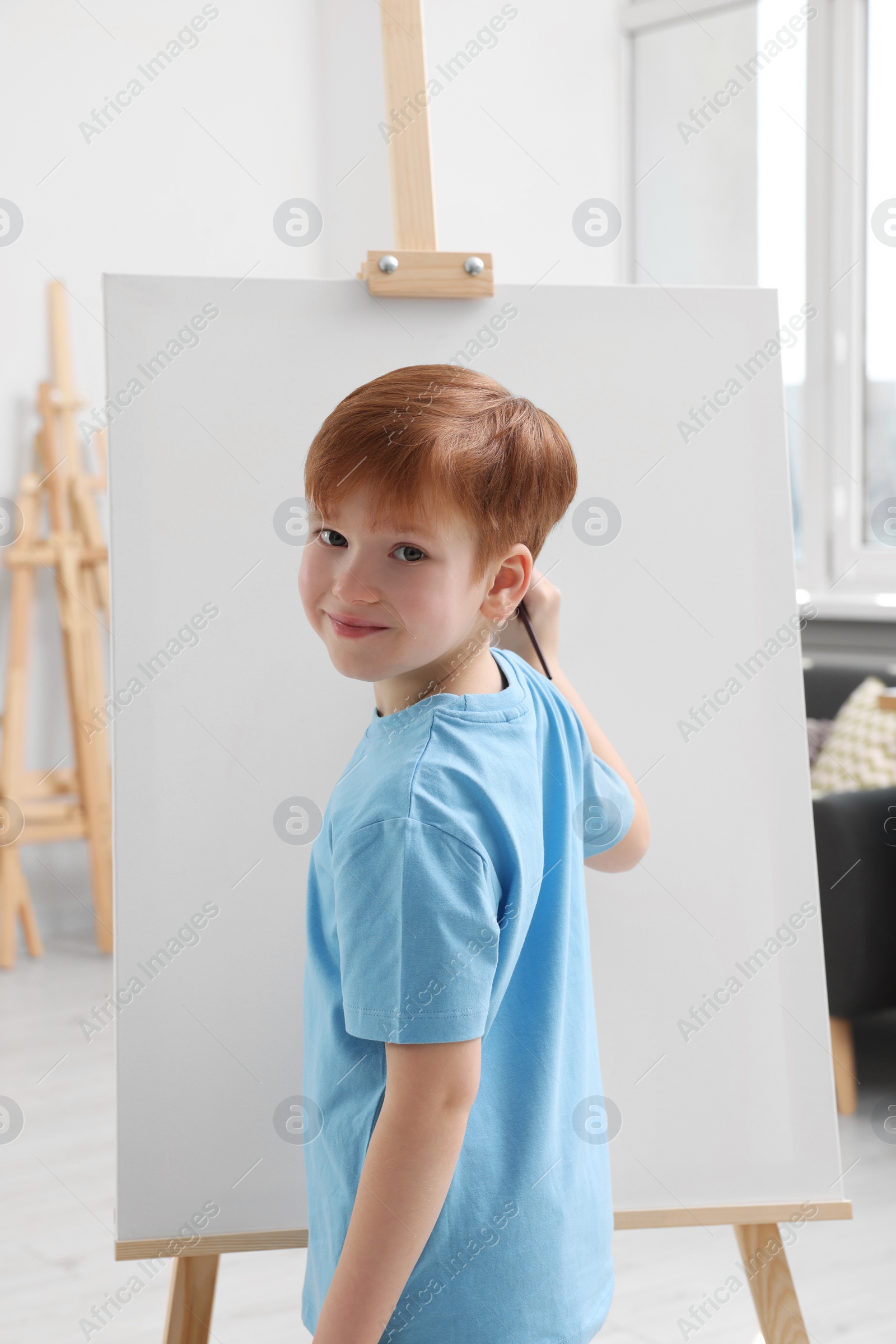 Photo of Little boy painting in studio. Using easel to hold canvas