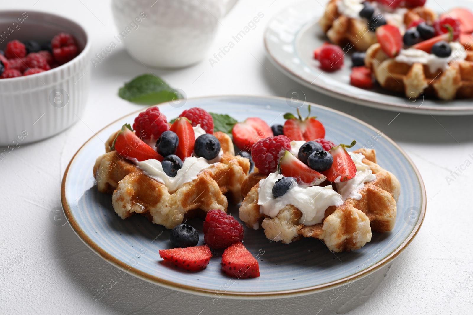 Photo of Delicious Belgian waffles with fresh berries and whipped cream on white table