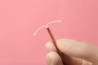 Doctor holding T-shaped intrauterine birth control device on pink background, closeup