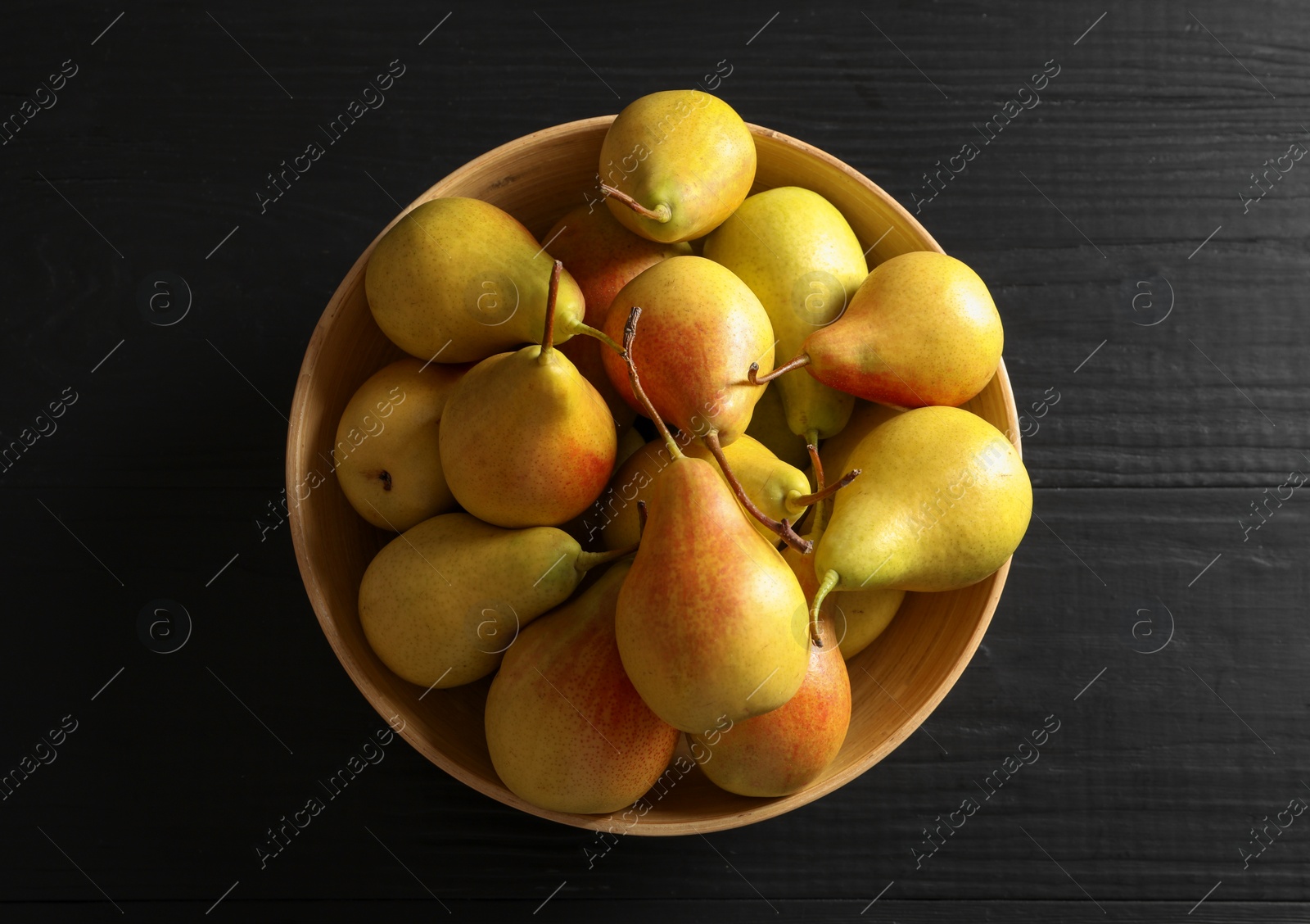 Photo of Bowl with ripe pears on black wooden background, top view