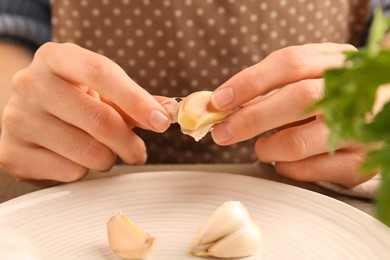 Woman peeling fresh garlic at table, closeup