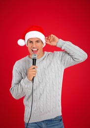 Happy man in Santa Claus hat singing with microphone on red background. Christmas music