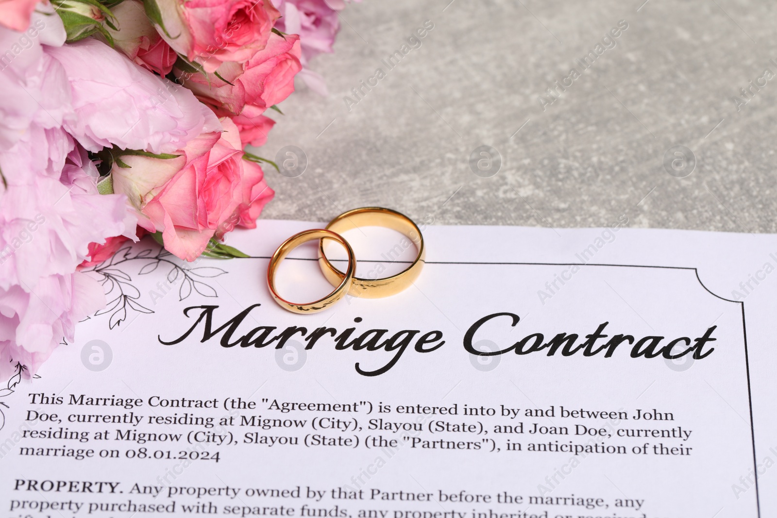 Photo of Marriage contract, golden wedding rings and flowers on grey table, closeup