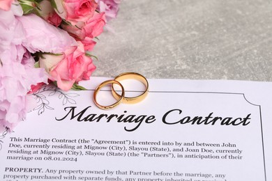 Photo of Marriage contract, golden wedding rings and flowers on grey table, closeup