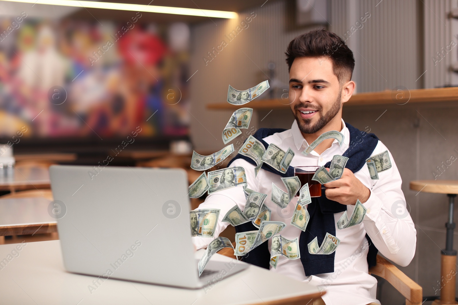 Image of Man with modern laptop and flying dollar banknotes at table indoors. People make money online