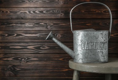 Vintage metal watering can on table against wooden background, space for text