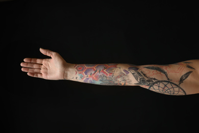 Photo of Woman with colorful tattoos on arm against black background, closeup