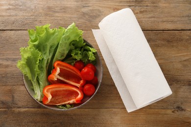 Photo of Bowl with fresh vegetables and roll of paper towels on wooden table, flat lay