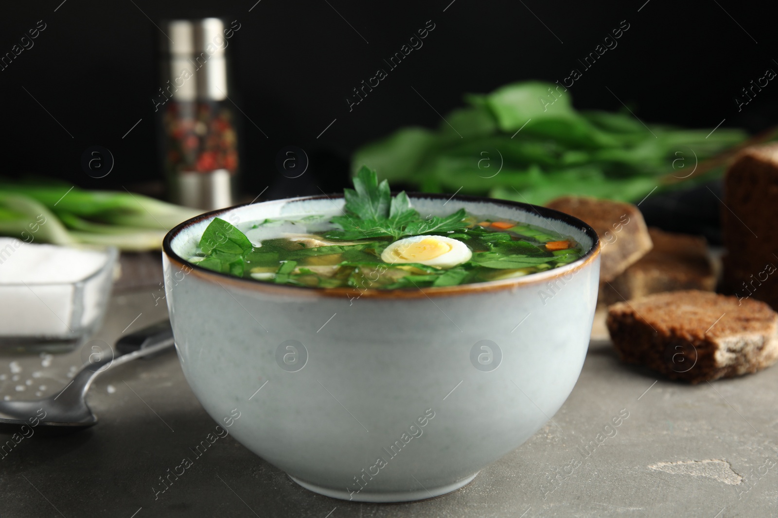Photo of Delicious sorrel soup with meat and egg served on grey table