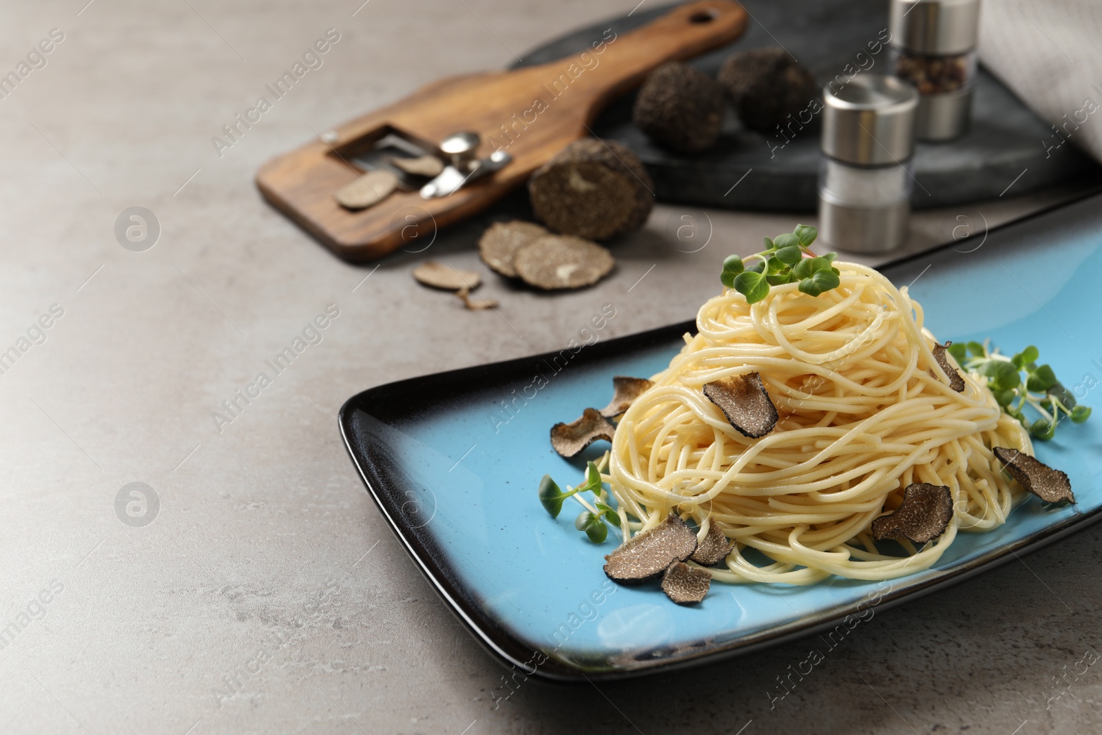 Photo of Delicious pasta with truffle slices and microgreens served on light grey table, space for text