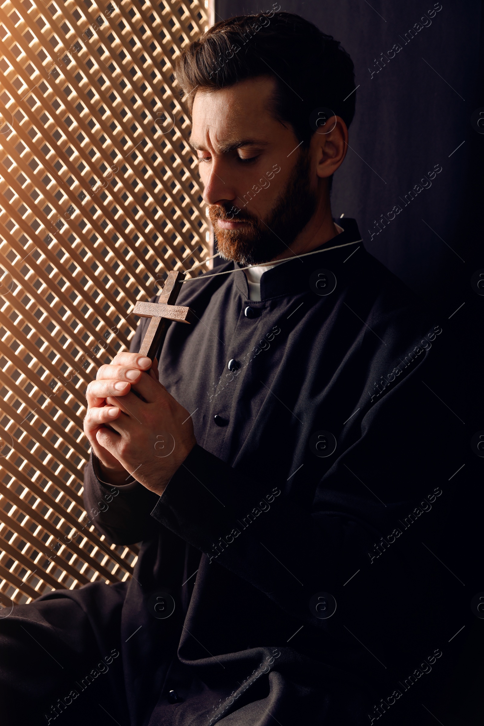 Photo of Catholic priest in cassock holding cross in confessional booth