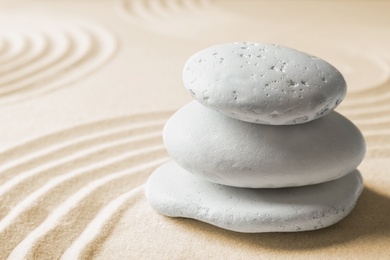 Stacked zen garden stones on sand with pattern, space for text. Meditation and harmony