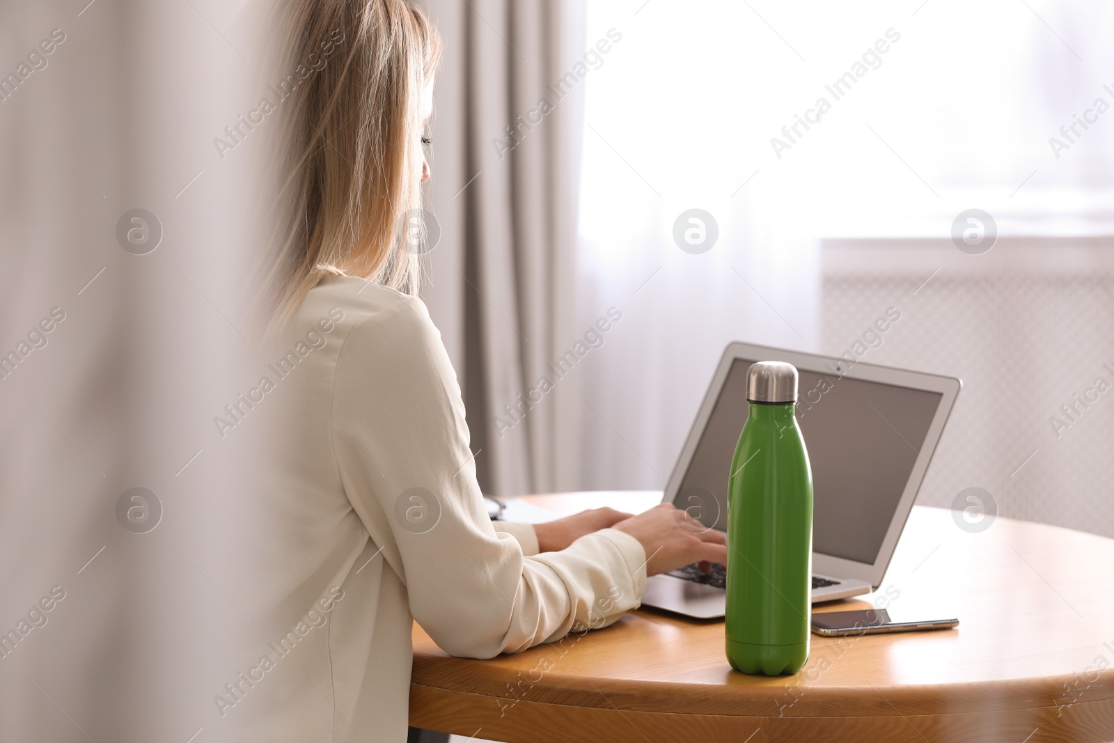 Photo of Woman with thermo bottle working at table in modern office, closeup