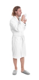 Young man in bathrobe with cup of drink on white background