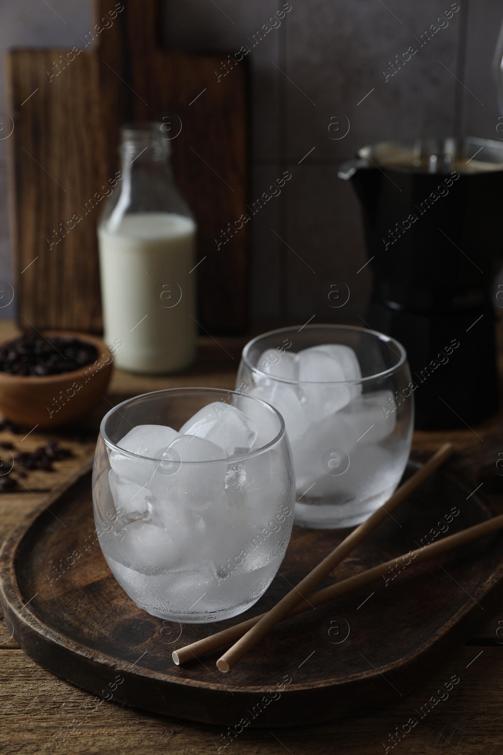 Photo of Making iced coffee. Ice cubes in glasses and straws on wooden table