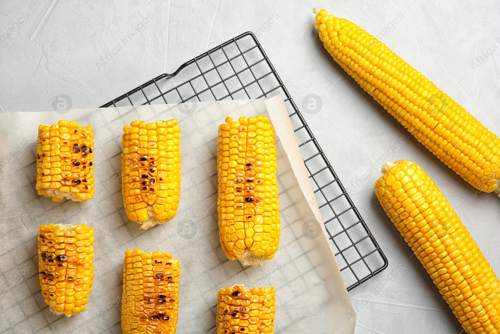 Photo of Cooling rack with grilled corn cobs on light background, top view