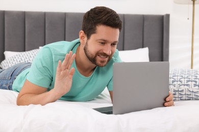 Happy man greeting someone during video chat via laptop in bedroom