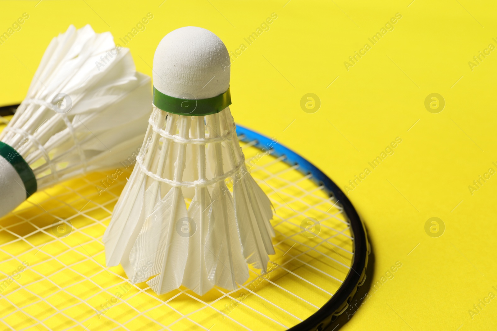 Photo of Feather badminton shuttlecocks and racket on yellow background, closeup