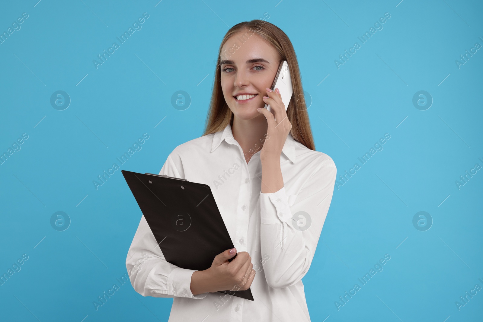 Photo of Happy secretary with clipboard talking on smartphone against light blue background