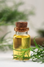 Bottle of essential oil and fresh tarragon leaves on white wooden table