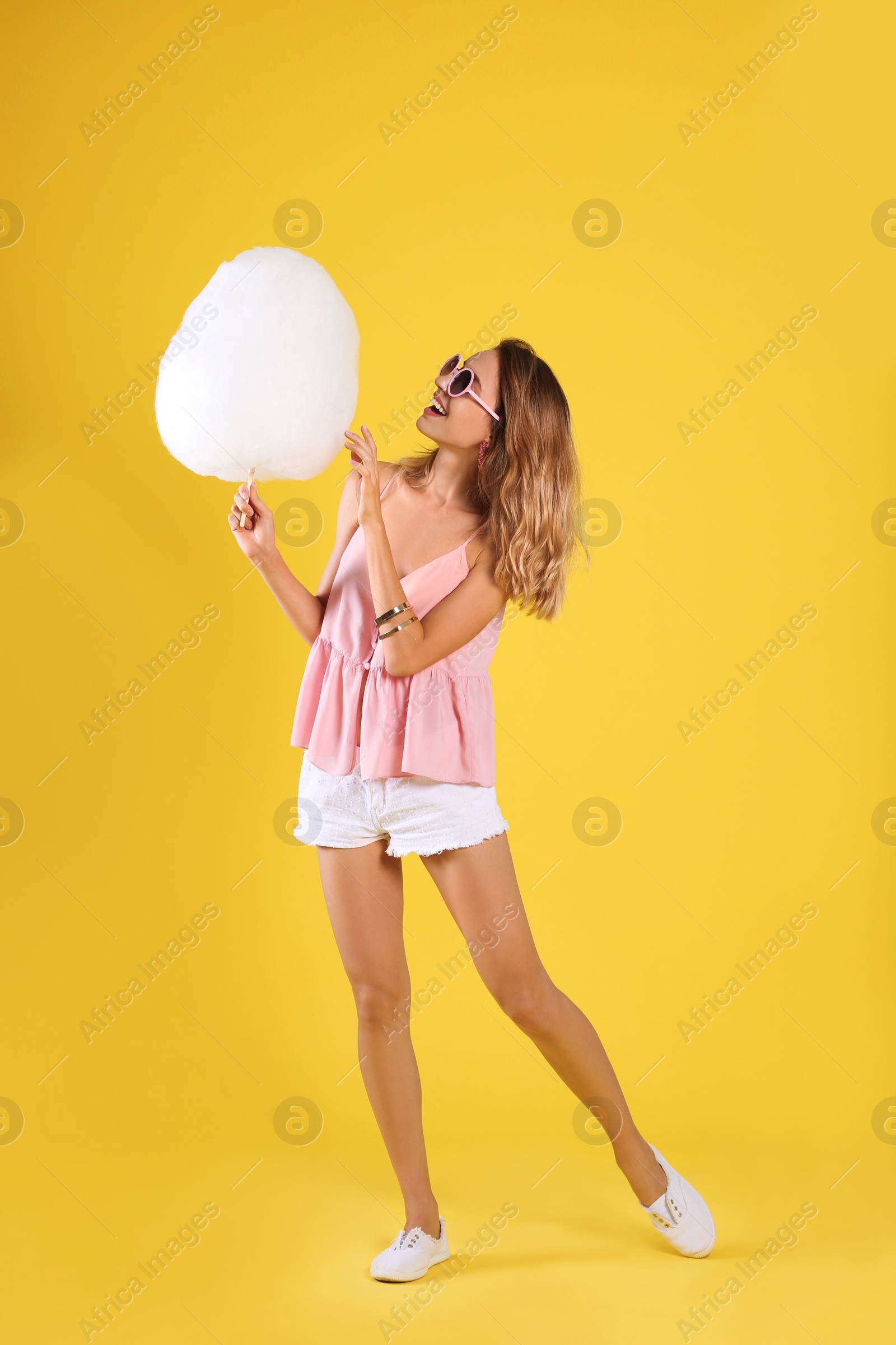 Photo of Happy young woman with cotton candy on yellow background