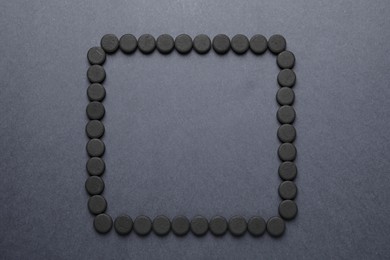 Photo of Frame of activated charcoal pills on grey background, flat lay with space for text. Potent sorbent