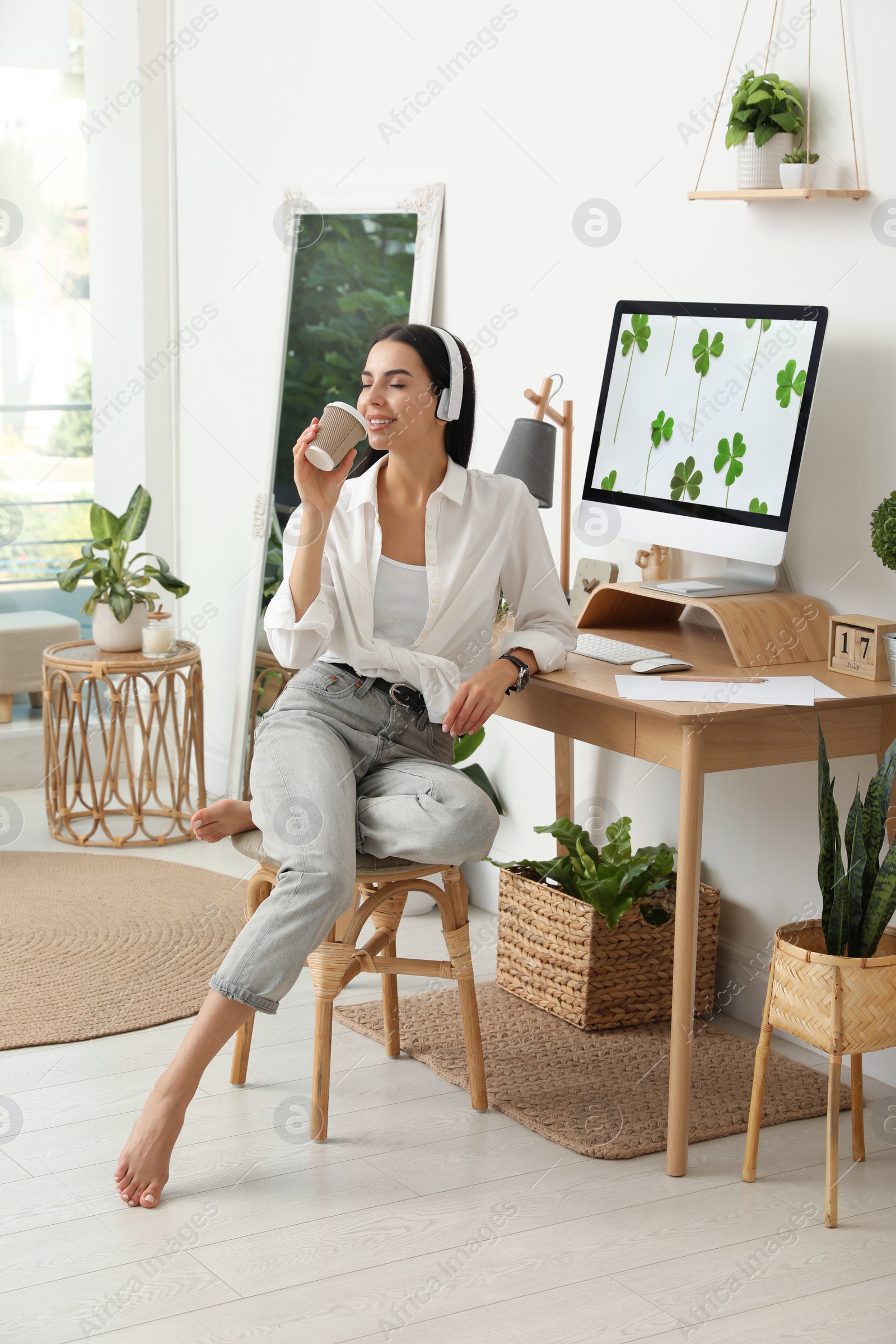 Photo of Young woman with cup of drink at table in room. Home office