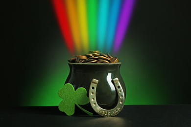 Pot with gold coins, horseshoe and clover on table against dark background. St. Patrick's Day