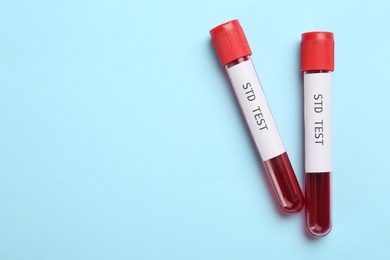 Photo of Tubes with blood samples and labels STD Test on light blue background, flat lay. Space for text