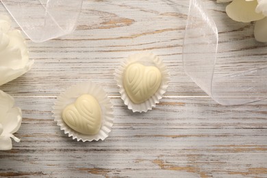 Delicious heart shaped chocolate candies and beautiful tulips on white wooden table, flat lay