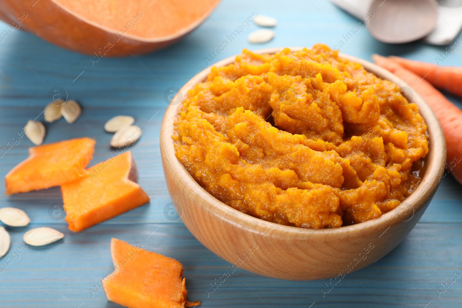 Photo of Bowl with tasty puree, carrots and pumpkin on light blue wooden table, closeup