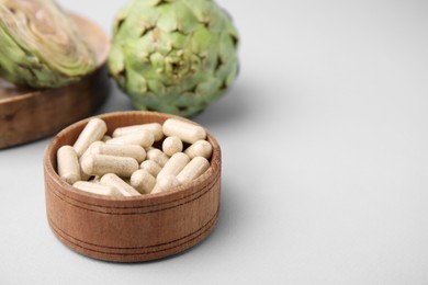 Photo of Bowl with pills and fresh artichokes on light grey background, closeup. Space for text