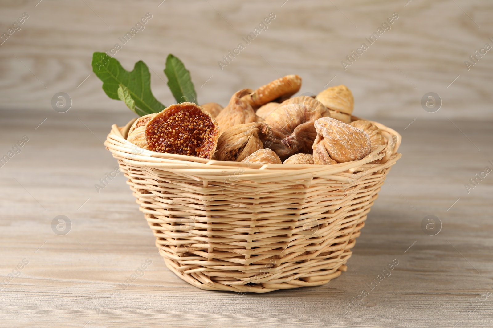 Photo of Wicker basket with tasty dried figs and green leaf on light wooden table