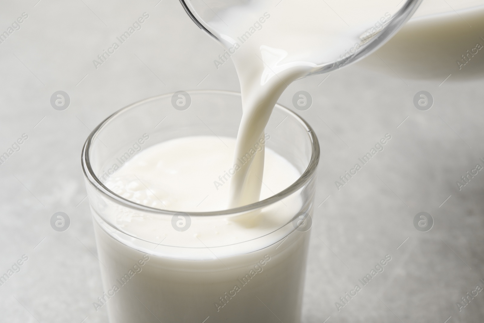 Photo of Pouring milk into glass on grey table, closeup