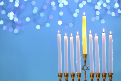 Photo of Hanukkah celebration. Menorah with burning candles on light blue background with blurred lights, space for text