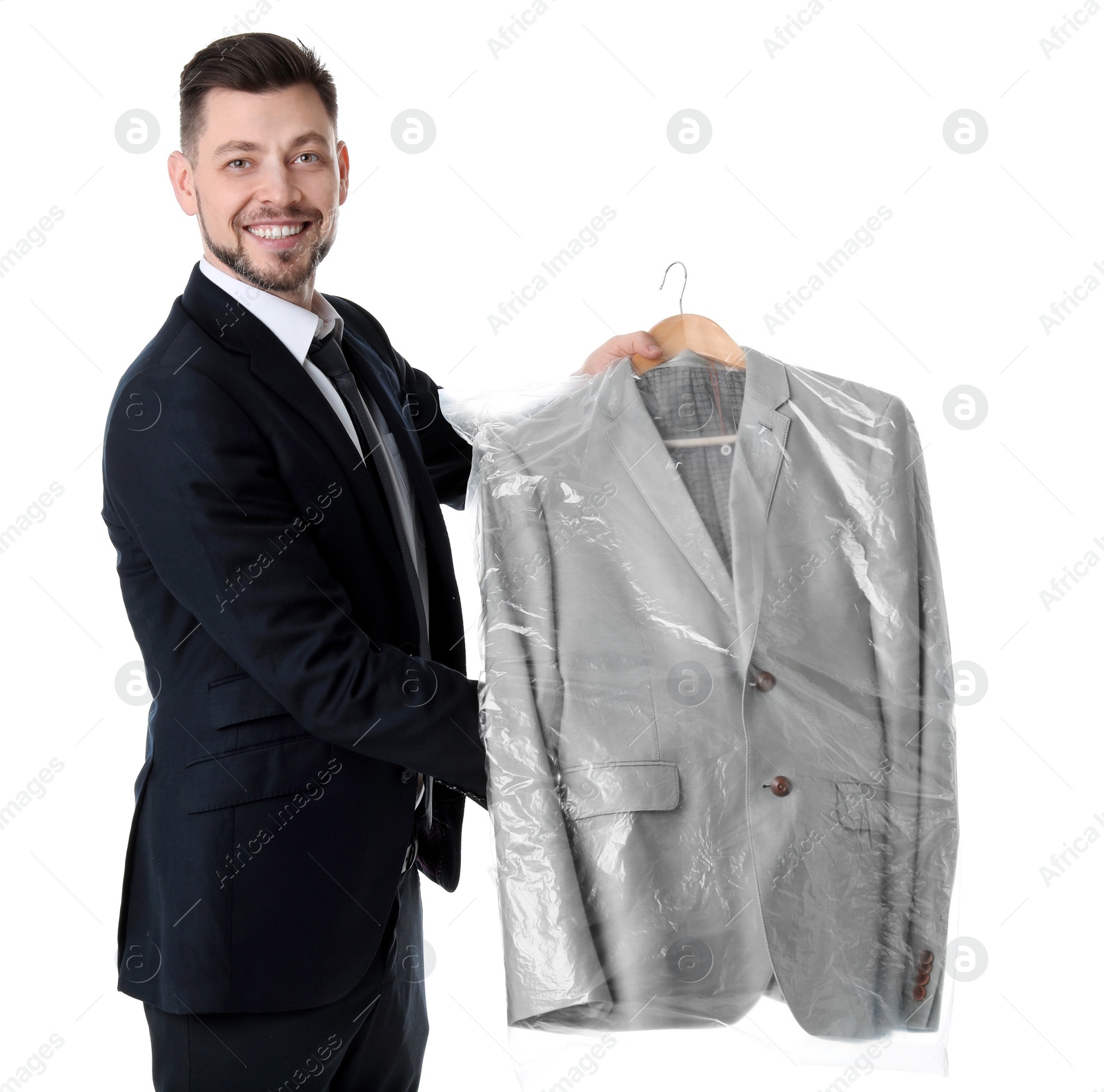 Photo of Young businessman holding hanger with jacket in plastic bag on white background. Dry-cleaning service