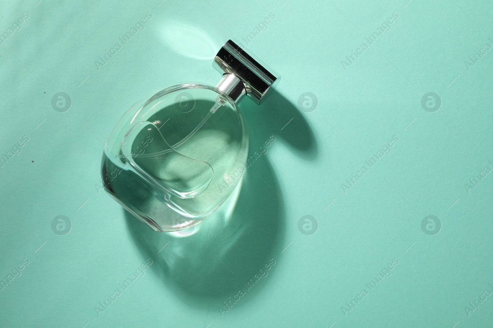 Photo of Luxury perfume in bottle on turquoise background, top view. Space for text