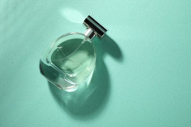 Luxury perfume in bottle on turquoise background, top view. Space for text