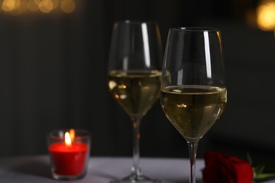 Photo of Glasses of white wine, burning candle and rose flower on table against blurred lights, space for text. Romantic atmosphere