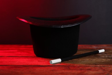 Photo of Black top hat and wand on wooden table. Magician equipment