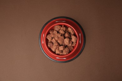 Photo of Wet pet food in feeding bowl on brown background, top view