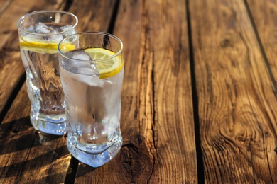 Photo of Glasses of refreshing drink with ice and lemon for hot summer day on wooden table, space for text