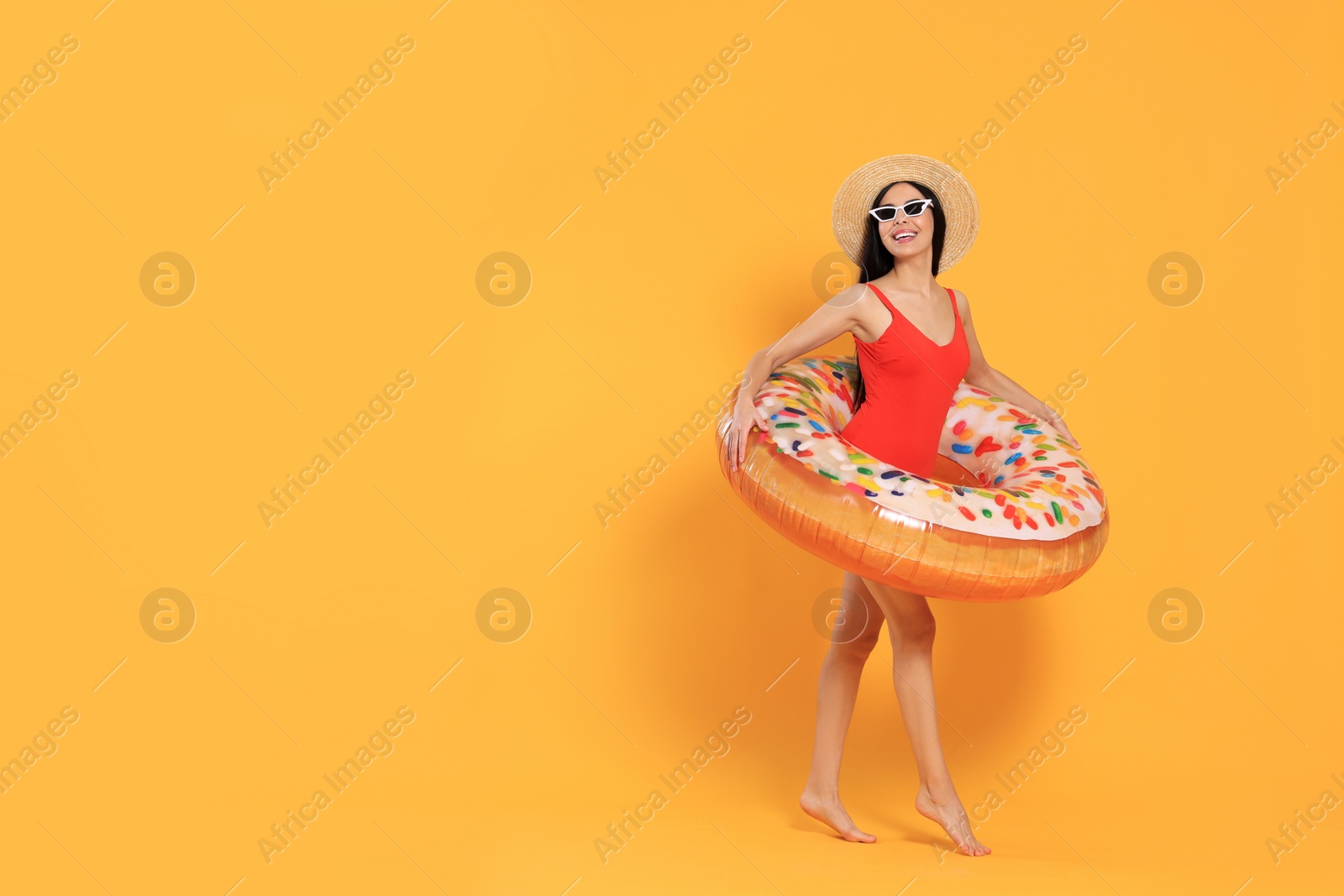 Photo of Happy young woman with beautiful suntan, hat, sunglasses and inflatable ring against orange background, space for text