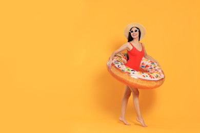 Happy young woman with beautiful suntan, hat, sunglasses and inflatable ring against orange background, space for text