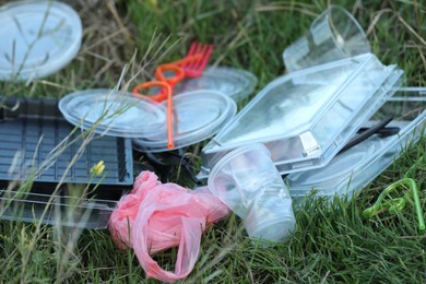 Photo of Used plastic tableware and bag on grass outdoors, closeup. Environmental pollution concept