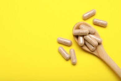 Photo of Many gelatin capsules and spoon on yellow background, flat lay. Space for text