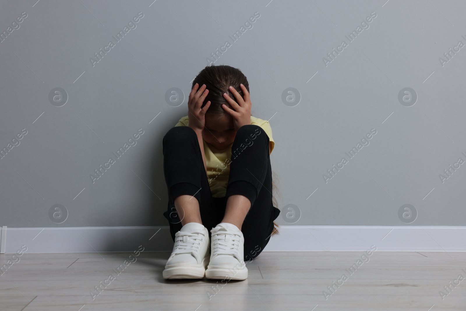 Photo of Child abuse. Upset girl sitting on floor near grey wall